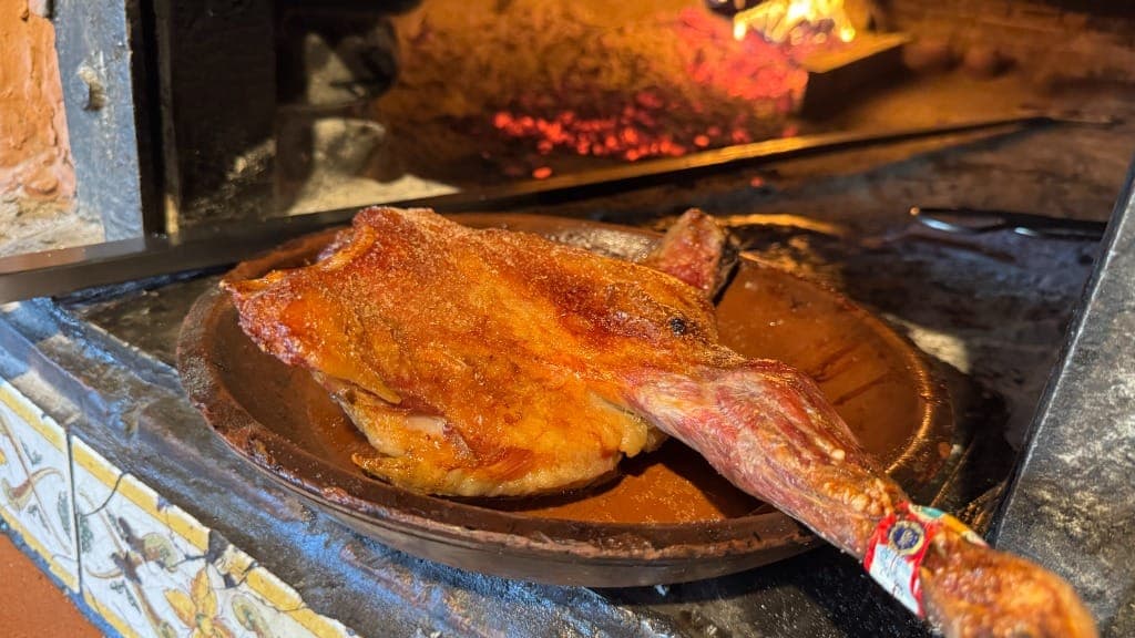 Cuarto de lechazo asado en cazuela de barro en el horno tradicional de leña